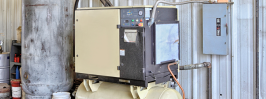 Industrial rotary screw air compressor with receiver tank and control panel in a manufacturing facility